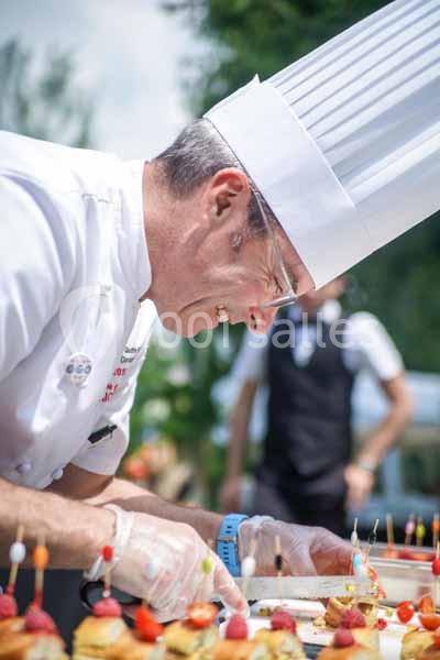 Un chef cuisinier en toque blanche prépare des amuse-bouches lors d'un événement en extérieur.
