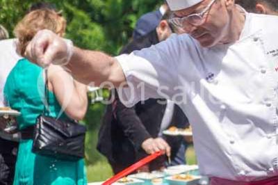 Boule croustillante sur lit de salade, garnie d'une framboise et décorée de sauce rouge sur assiette blanche.