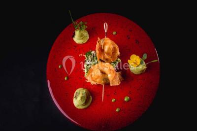 Boule croustillante sur lit de salade, garnie d'une framboise et décorée de sauce rouge sur assiette blanche.