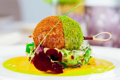 Boule croustillante sur lit de salade, garnie d'une framboise et décorée de sauce rouge sur assiette blanche.