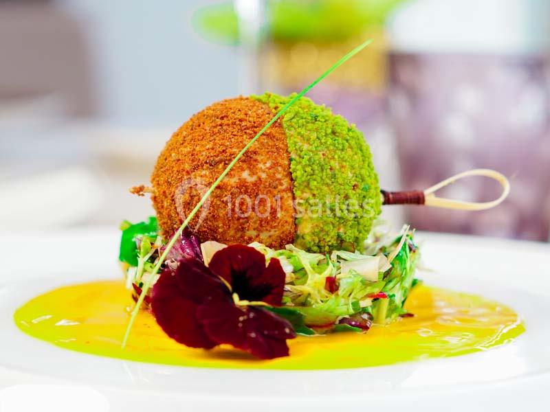 Boule panée bicolore sur lit de salade, décorée de fleurs comestibles et nappée d'une sauce jaune.