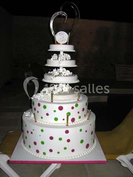 Gâteau de mariage à plusieurs étages décoré de pois colorés et de fleurs blanches, avec un ornement en cœur au sommet.