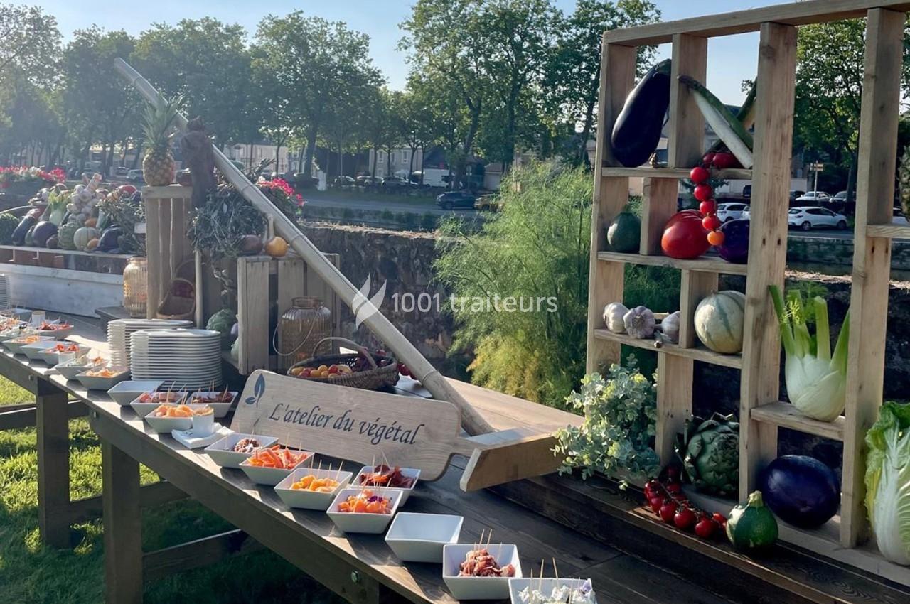 Buffet en plein air avec légumes frais, fruits et plats disposés sur une table en bois, entourée de verdure.