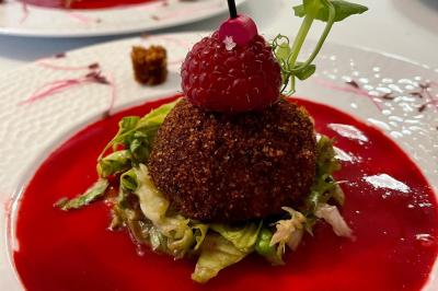 Boule croustillante sur lit de salade, garnie d'une framboise et décorée de sauce rouge sur assiette blanche.