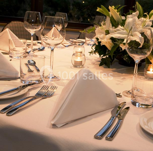 Table élégamment dressée avec serviettes pliées, verres à pied, couverts en métal et centre de table floral.