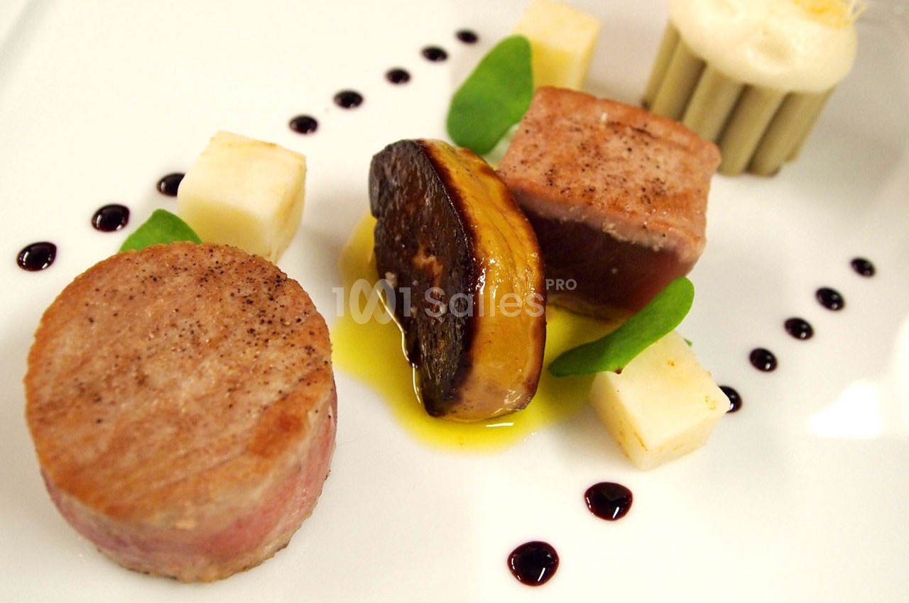 Assiette gastronomique avec viande, foie gras, cubes de fromage, sauce et décor de points de réduction balsamique.