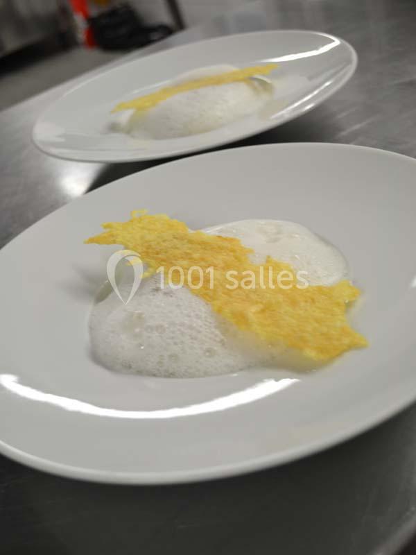 Deux assiettes blanches contenant une mousse blanche et une fine tuile dorée, posées sur une surface métallique.