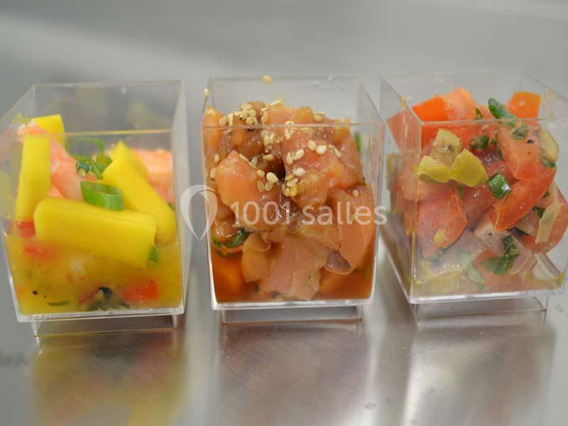 Trois verrines contenant des préparations colorées à base de fruits et de poisson, présentées sur une surface métallique.