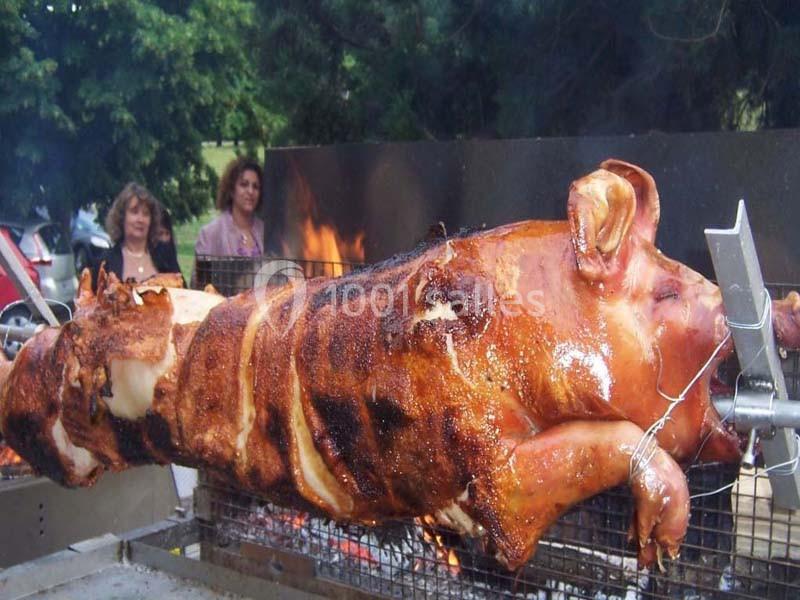 Un cochon entier rôti à la broche sur un barbecue en plein air, avec des personnes en arrière-plan.