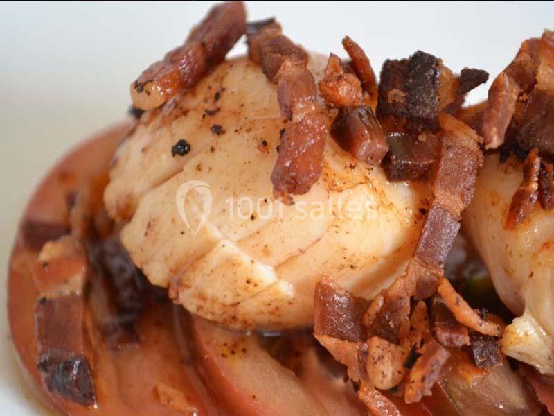 Noix de Saint-Jacques poêlées garnies de morceaux de bacon croustillants, servies sur un lit de légumes.