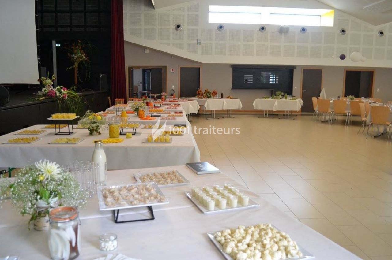 Buffet dressé dans une grande salle lumineuse, avec tables garnies de plats variés et décorations florales.