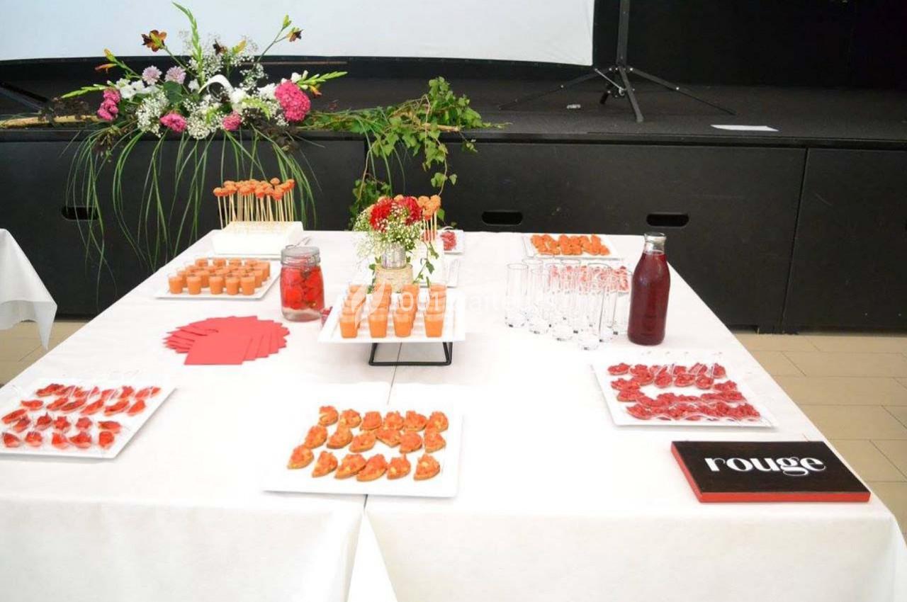 Table dressée avec des verrines, canapés, brochettes et boissons, décorée de fleurs et serviettes rouges.