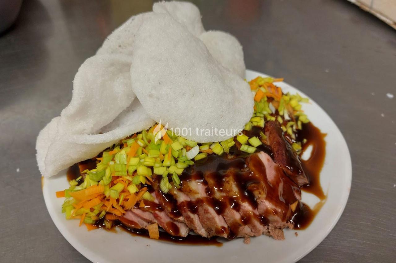 Assiette de magret de canard tranché, nappé de sauce, garni de légumes émincés et accompagné de chips de crevettes.