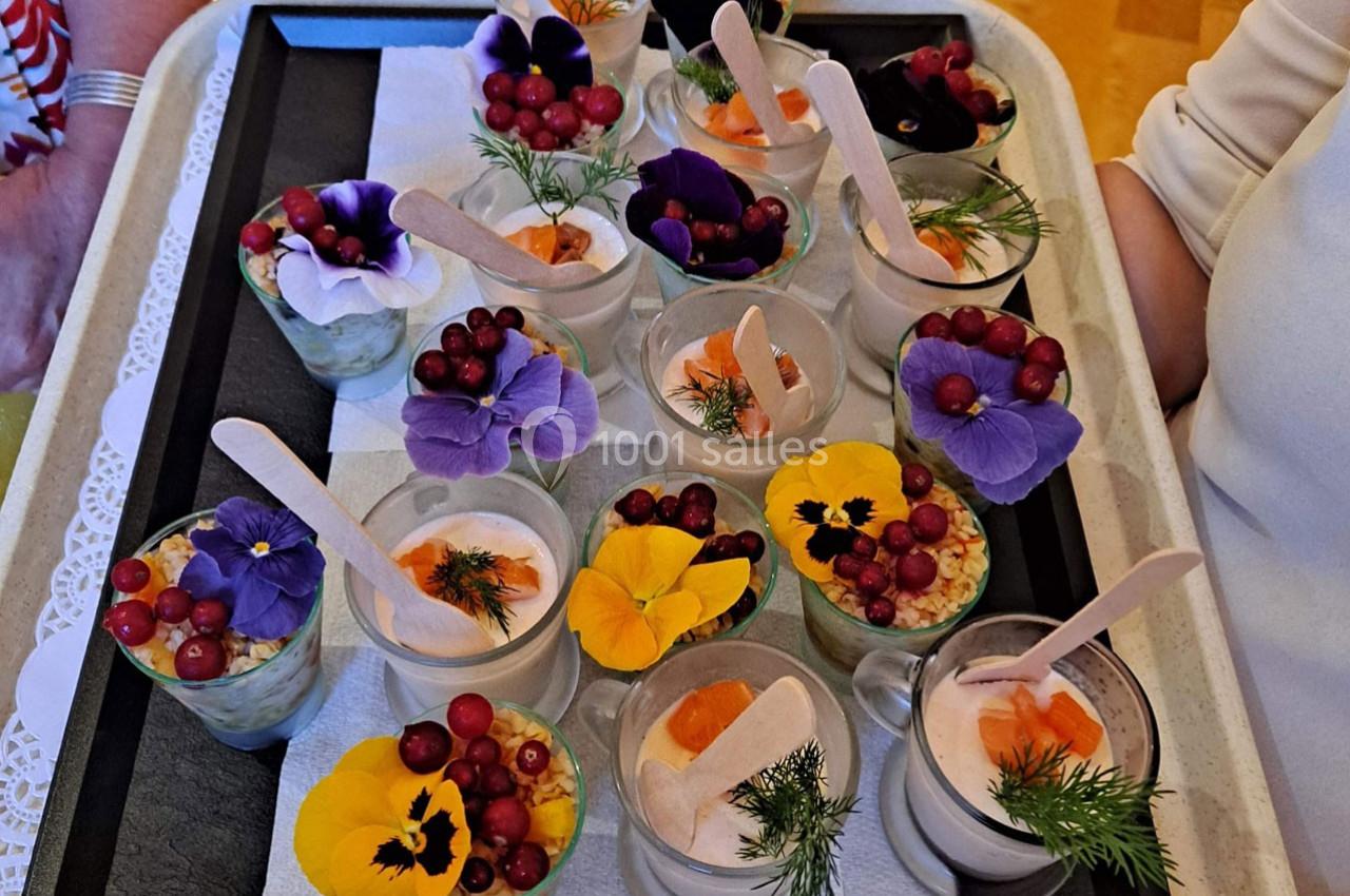 Plateau de verrines décorées de fleurs comestibles, baies rouges et herbes fraîches, présenté sur un fond clair.