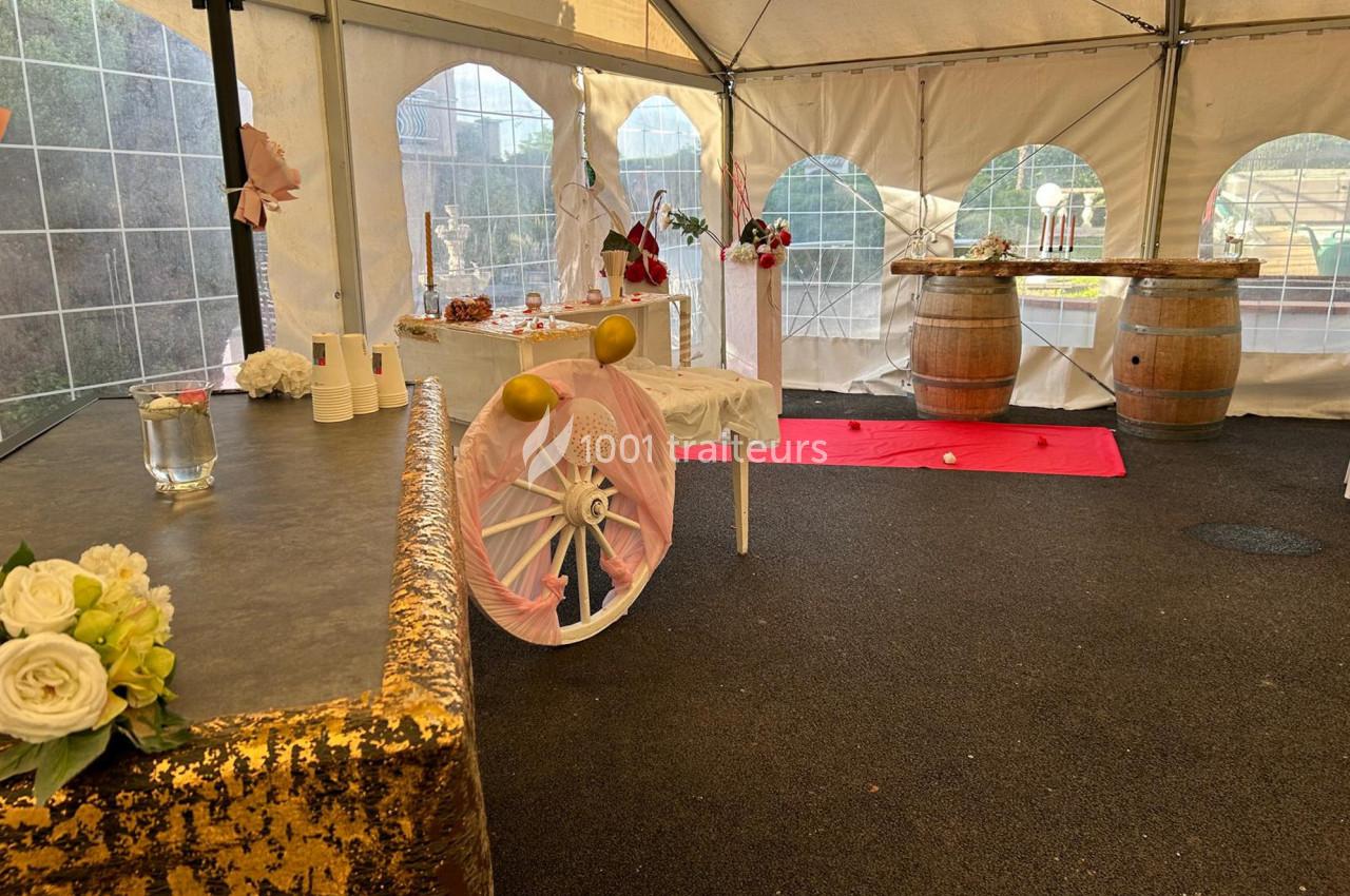 Décoration d'une tente événementielle avec tables ornées, barils en bois, fleurs et ballons dans un espace extérieur.
