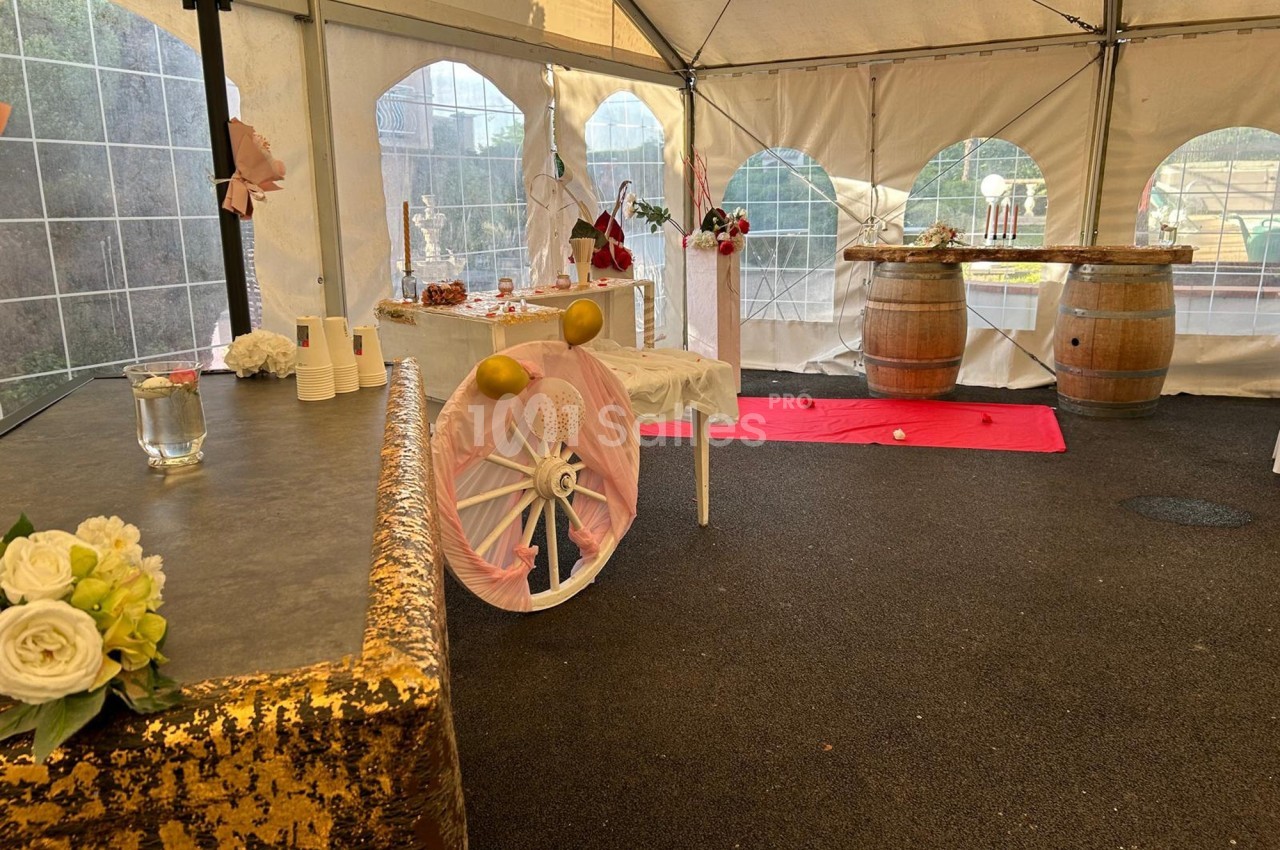 Décoration d'une tente événementielle avec tables ornées, barils en bois, fleurs et ballons dans un espace extérieur.