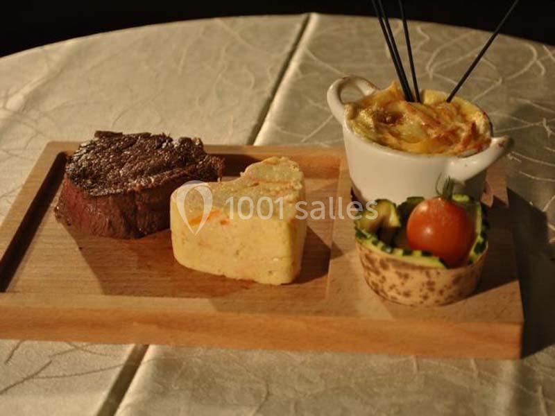 Assiette en bois avec un steak, une purée en forme de cœur, un gratin en ramequin et une garniture de légumes.