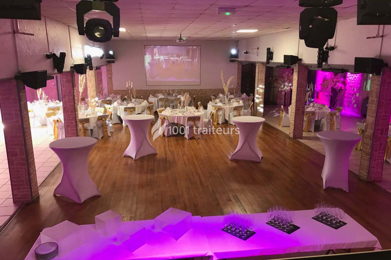 Salle de réception décorée avec des tables rondes, nappes blanches et éclairage rose pour un événement festif.