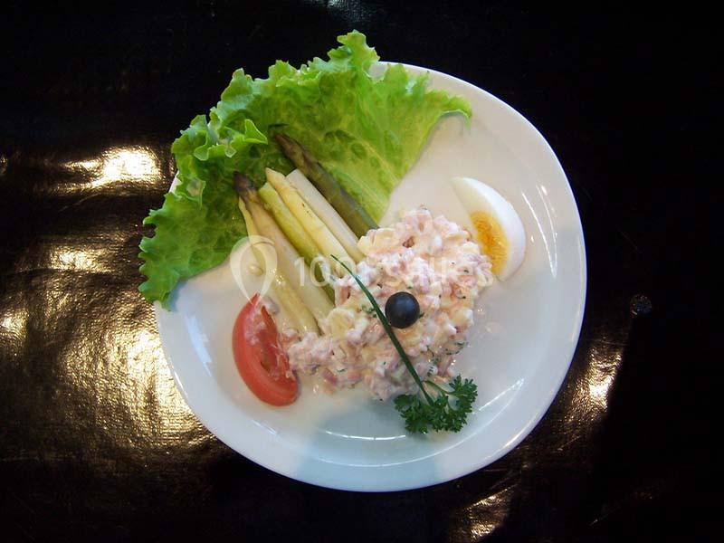 Assiette garnie d'asperges, salade verte, tomate, œuf dur, mélange crémeux et olive noire sur fond noir.