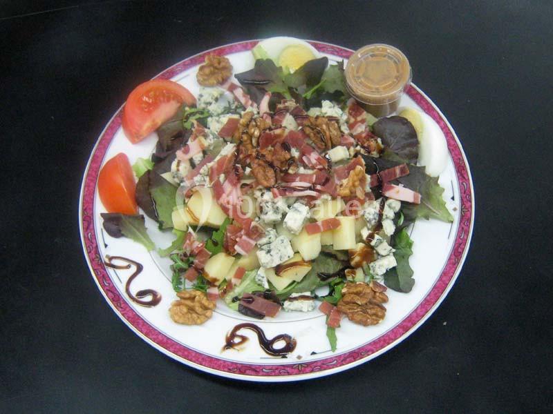 Assiette de salade composée avec noix, fromage bleu, pommes, bacon, tomates, œufs et vinaigrette en accompagnement.