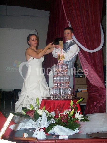 Un couple en tenue de mariage verse du champagne dans une pyramide de verres, entouré de décorations rouges et blanches.