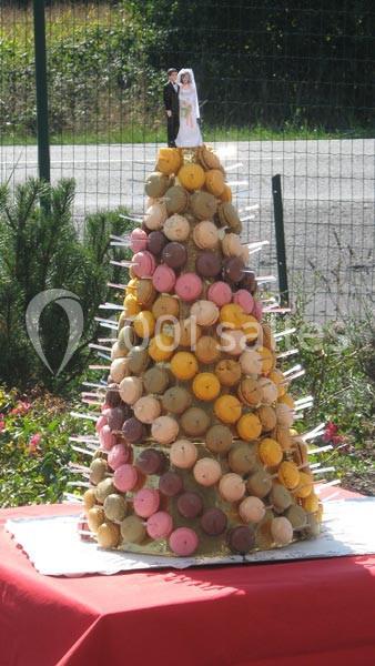 Pyramide de macarons colorés surmontée de figurines de mariés, présentée sur une table rouge en extérieur.