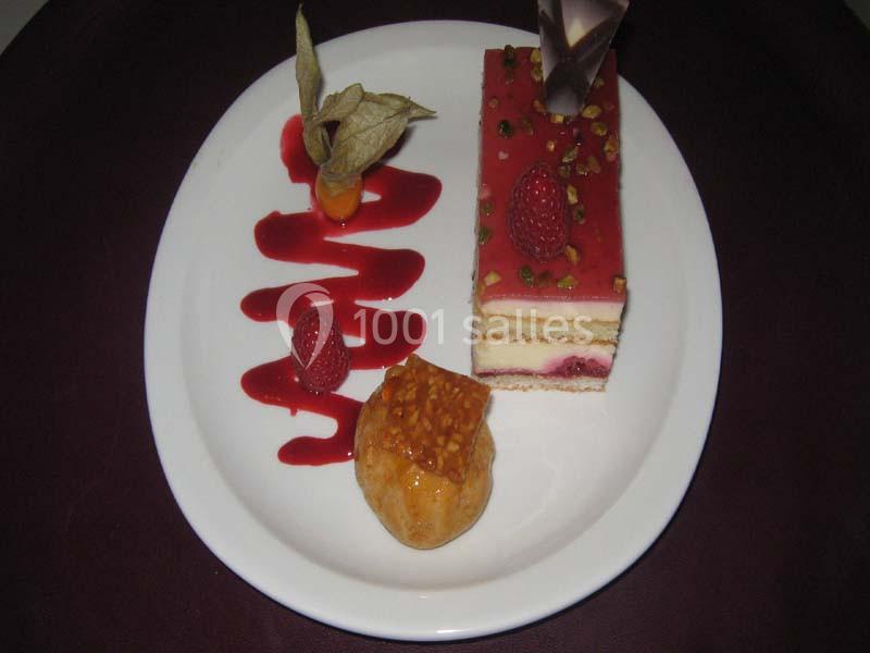 Assiette avec un gâteau aux fruits rouges, un coulis décoratif, une physalis et une bouchée caramélisée.
