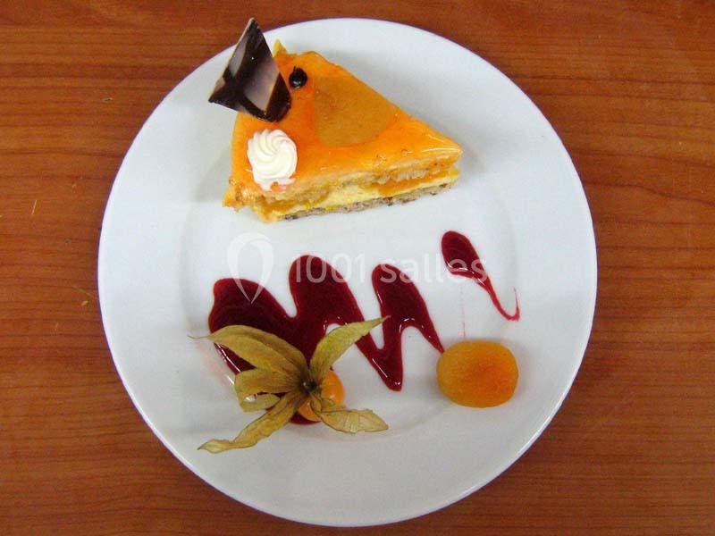 Part de gâteau à l'orange décorée de chocolat, chantilly et physalis, accompagnée de coulis rouge sur une assiette blanche.