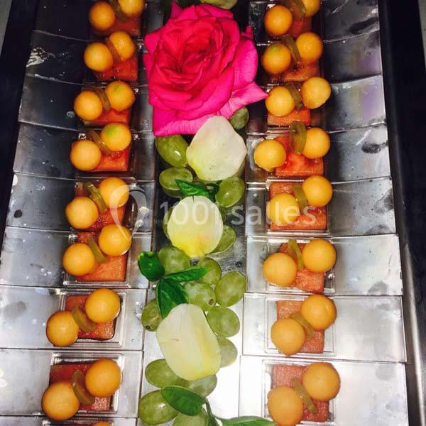 Plateau de desserts avec des billes de melon, raisins verts, morceaux de pastèque et une rose décorative au centre.