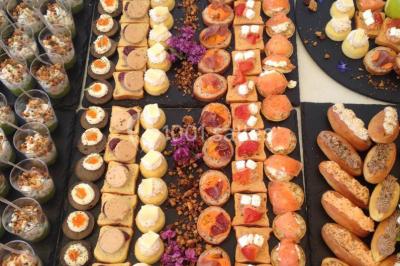 Plateau de bouchées variées comprenant verrines, toasts garnis, mini-sandwichs et décorations florales.