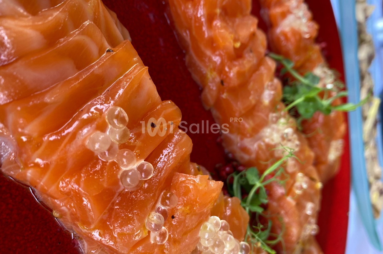 Tranches de saumon cru garnies de perles de citron et de micro-pousses, présentées sur un plat rouge.