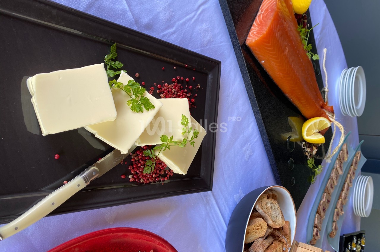Plateau avec du beurre, du saumon fumé, des tranches de pain et des garnitures sur une nappe violette.