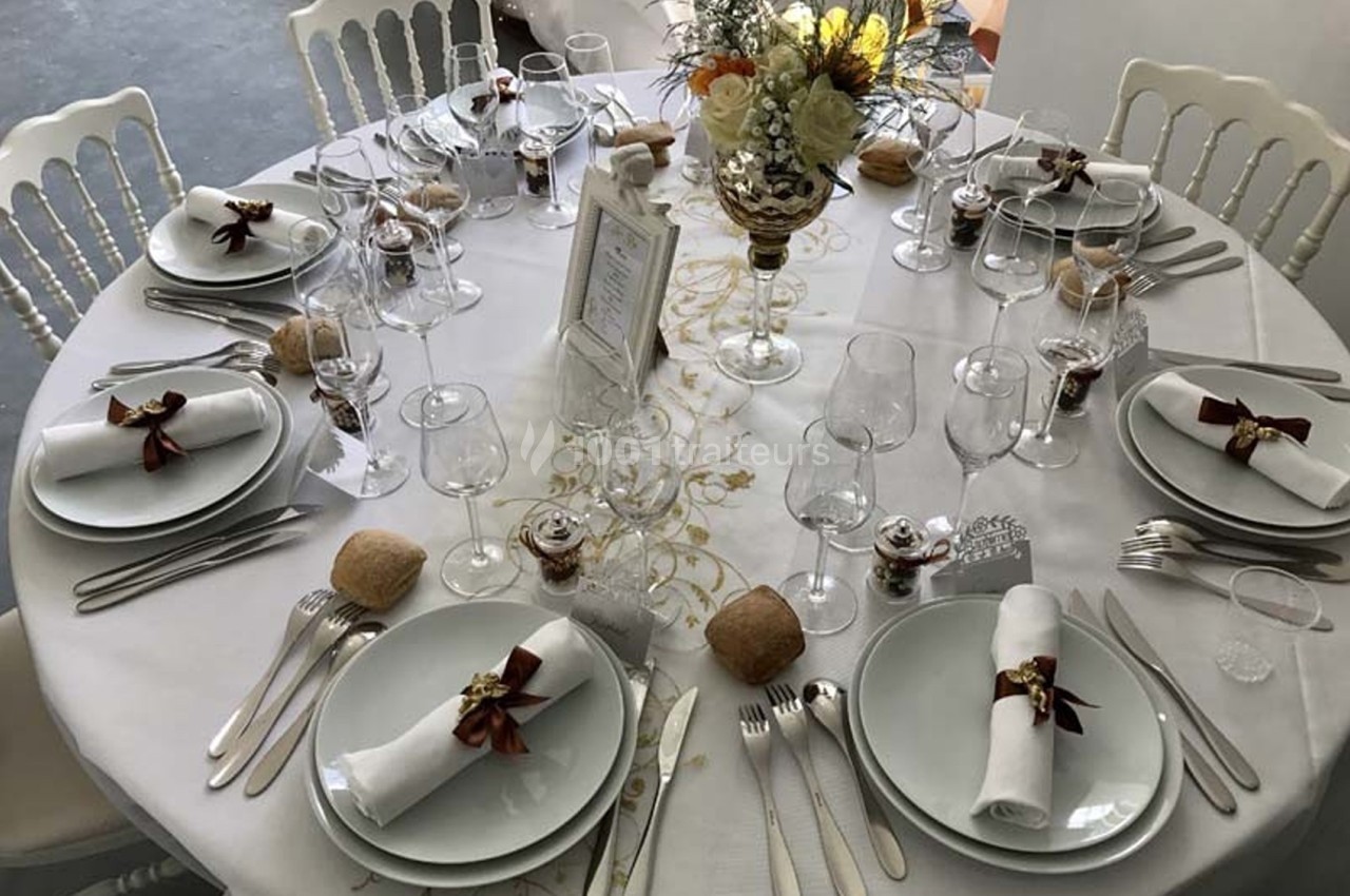 Table ronde élégamment dressée avec nappes blanches, couverts alignés, verres, serviettes roulées et décoration florale…