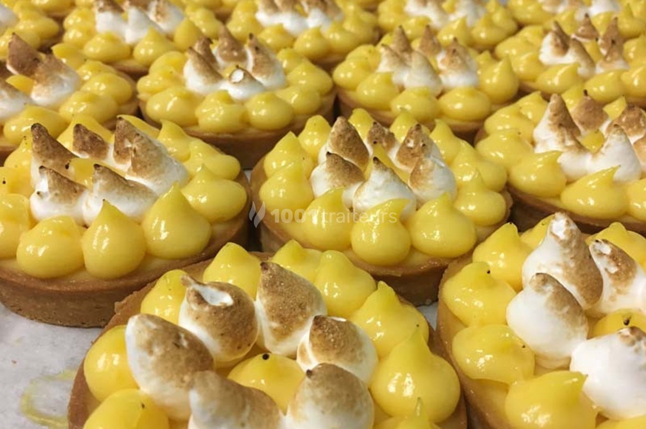 Tartelettes au citron garnies de meringue dorée alignées sur un plan de travail.