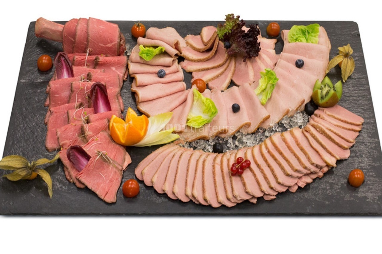 Plateau de charcuterie froide avec tranches de viande variées, décoré de fruits, légumes et feuilles de salade.