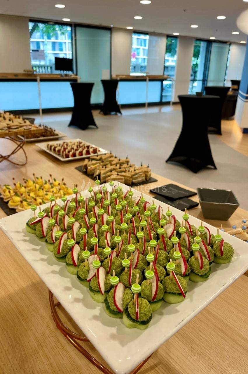 Plateau de bouchées apéritives vertes garnies de radis, disposé sur une table dans une salle de réception lumineuse.