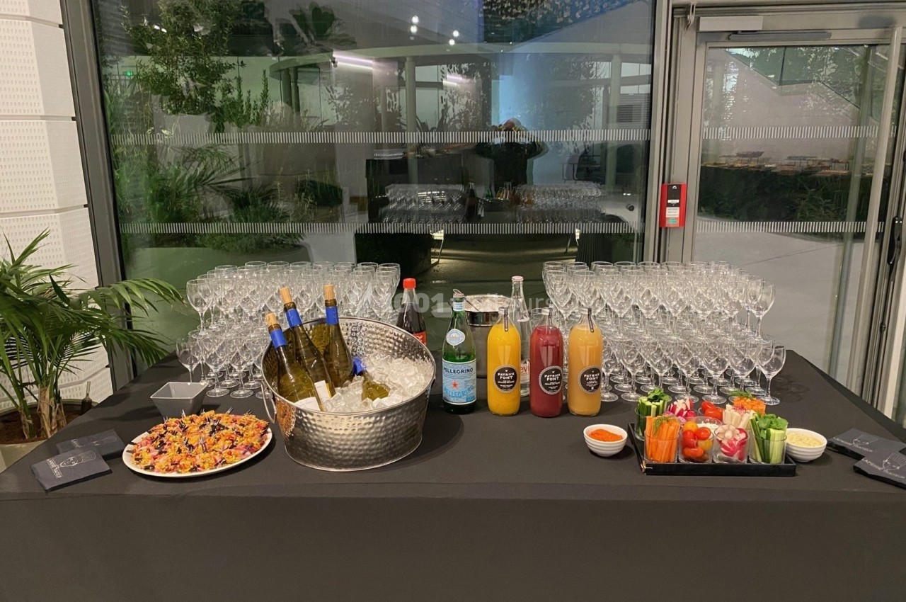 Table de réception avec verres, bouteilles de vin dans un seau, jus de fruits, sodas, légumes et amuse-bouches.