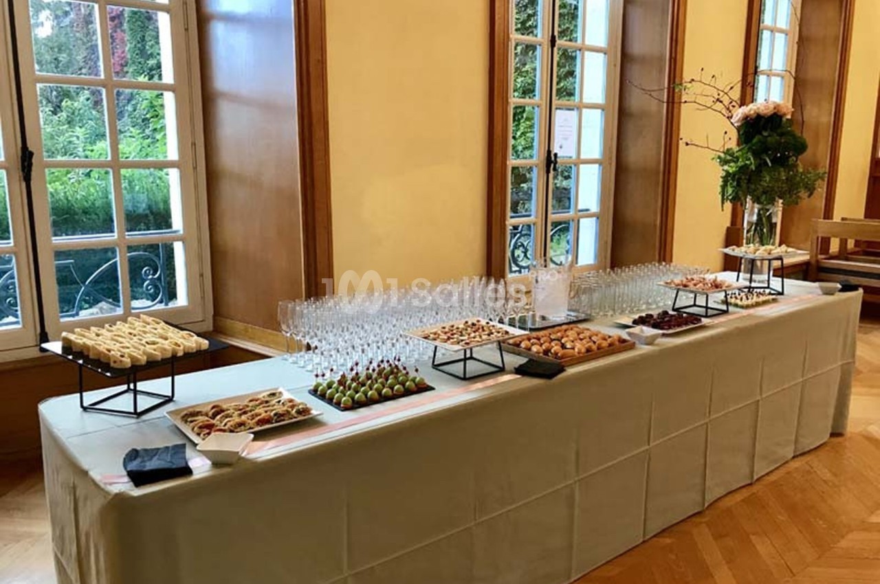 Table dressée avec des amuse-bouches variés, des verres vides et une décoration florale, dans une salle lumineuse.