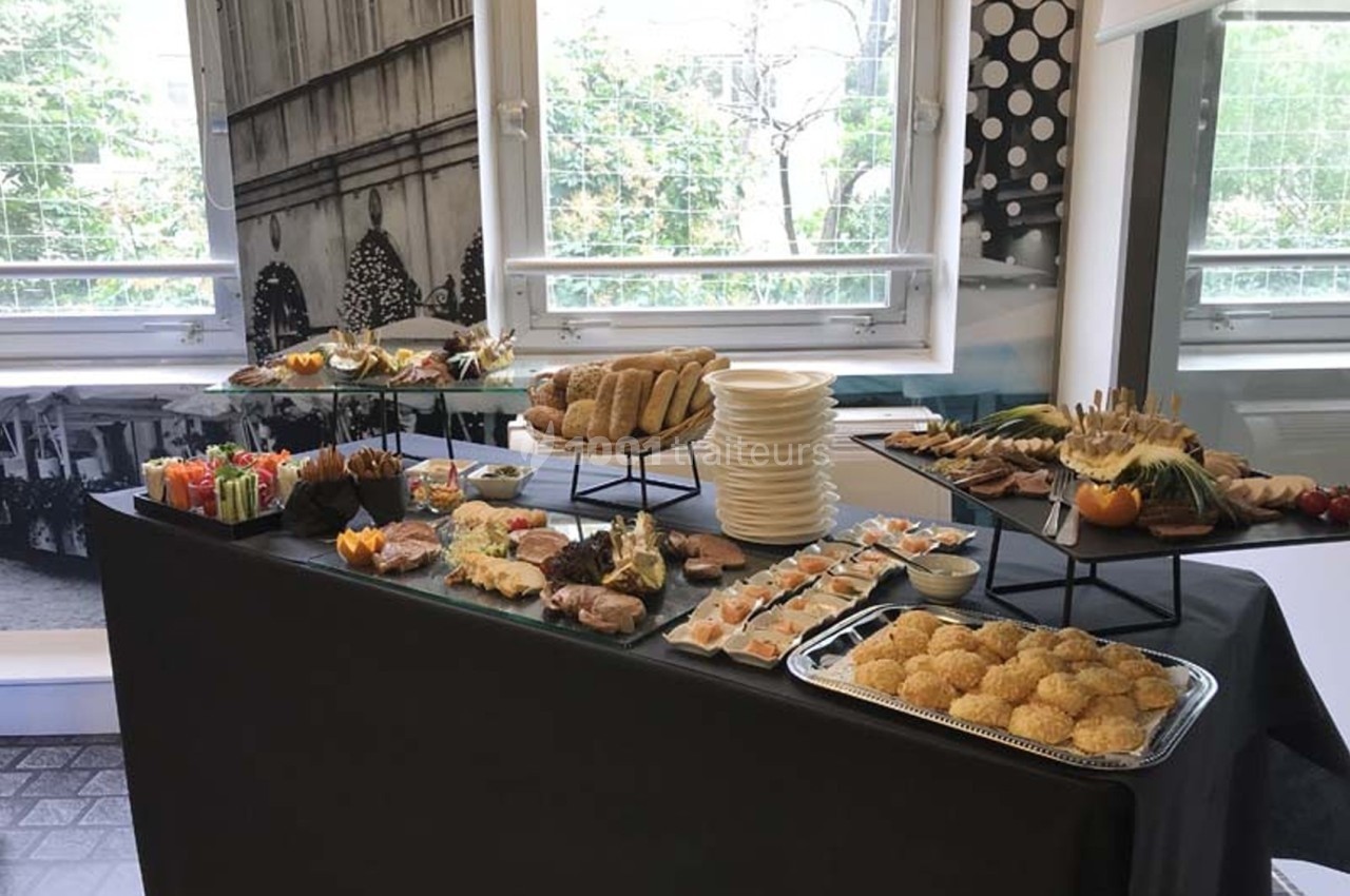 Buffet varié avec viennoiseries, fruits, légumes, pains et amuse-bouches disposés sur une table noire.