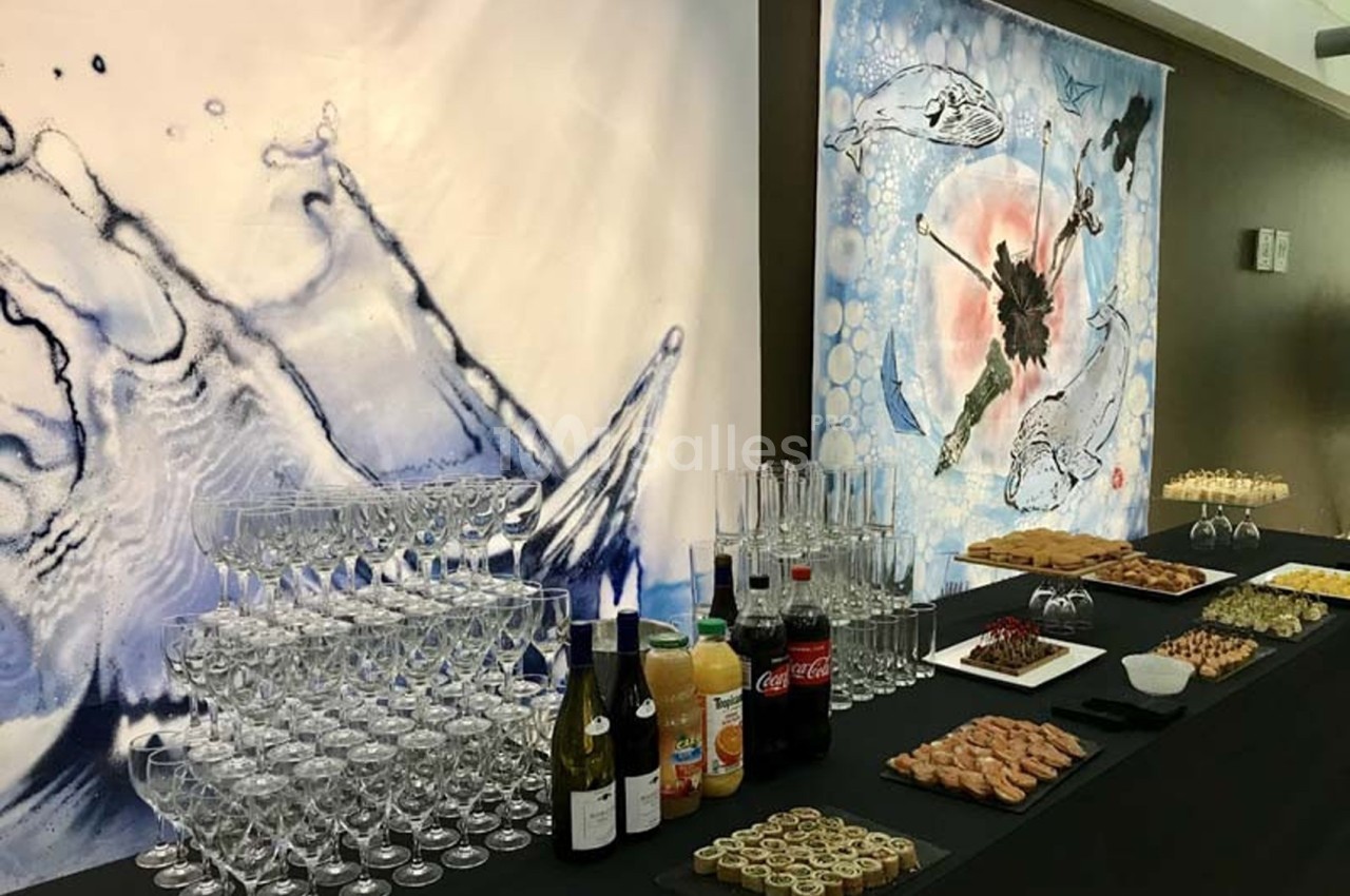 Table de buffet avec boissons, verrerie, amuse-bouches variés et décorations murales artistiques en arrière-plan.
