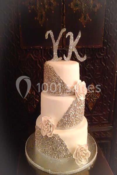 Gâteau de mariage à trois étages décoré de roses blanches, strass argentés et initiales ’YK’ scintillantes.