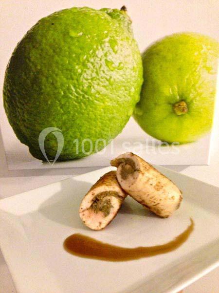 Deux citrons verts en arrière-plan avec un plat contenant des morceaux roulés garnis et une sauce en premier plan.