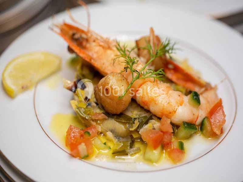 Assiette de crevettes et noix de Saint-Jacques servies sur un lit de légumes avec une tranche de citron.