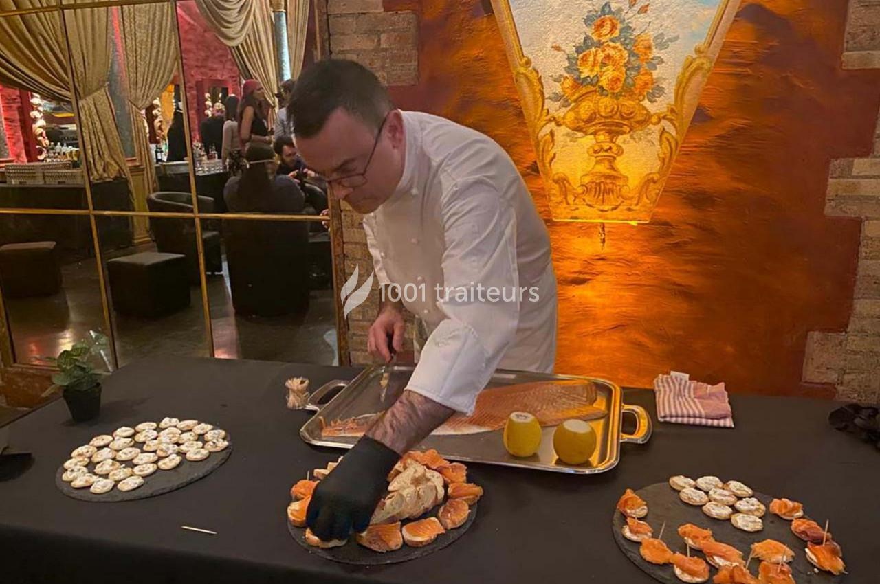Un chef prépare des plats raffinés sur une table décorée, avec des assiettes de bouchées et un fond élégant.