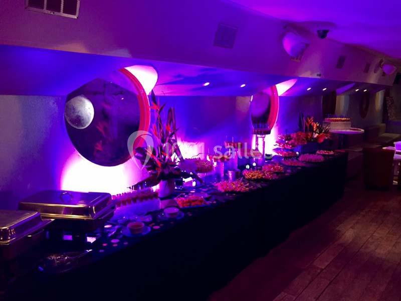 Buffet illuminé par des lumières violettes, disposé dans une salle avec miroirs ronds et décorations florales.