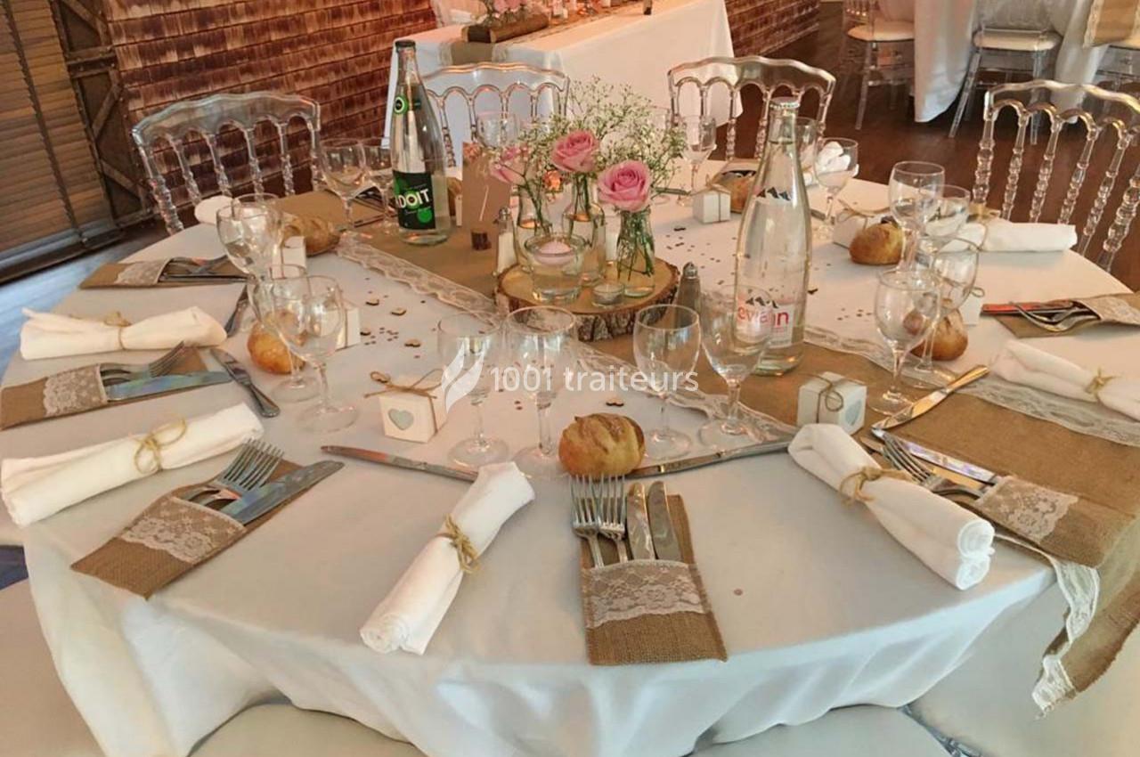 Table de réception décorée avec nappes blanches, couverts élégants, fleurs, bouteilles et petits pains.