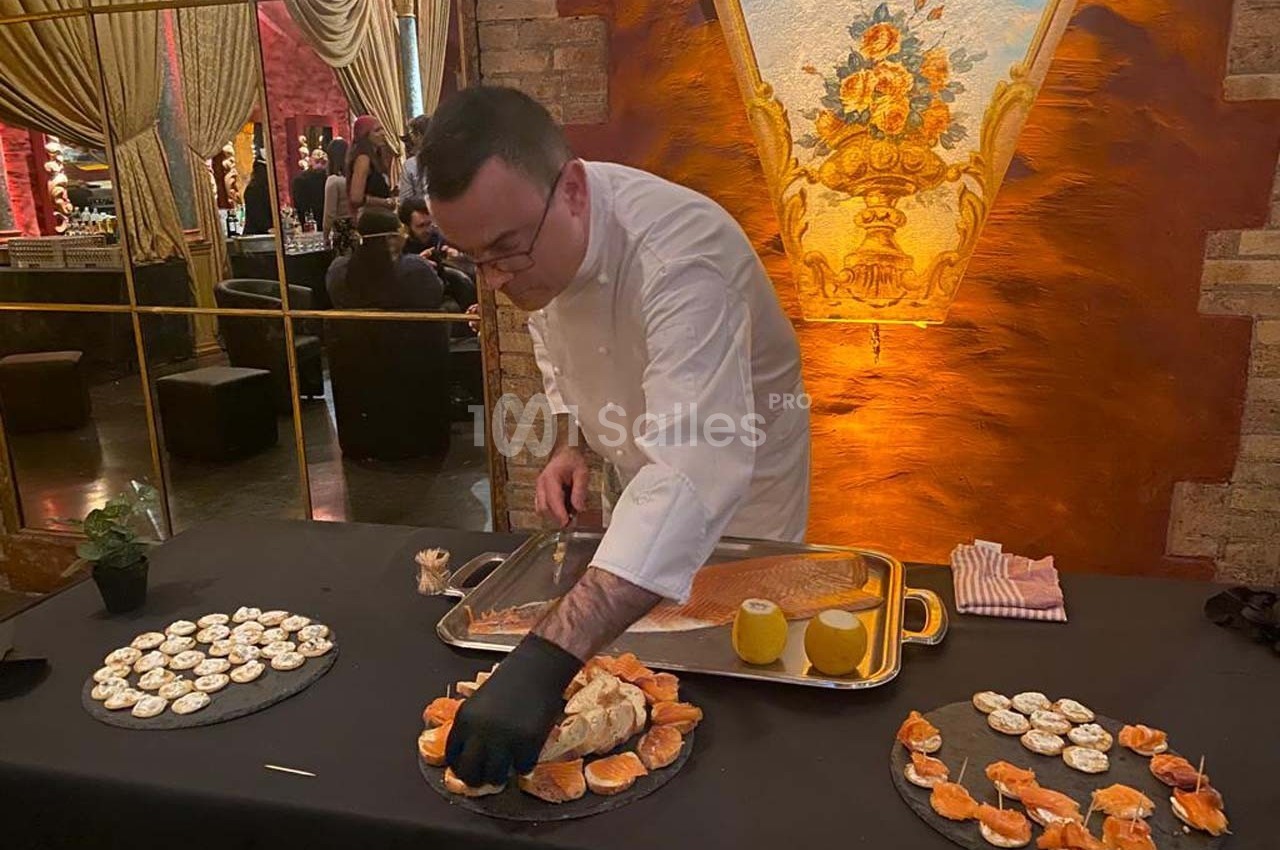 Un chef prépare des plats raffinés sur une table décorée, avec des assiettes de bouchées et un fond élégant.