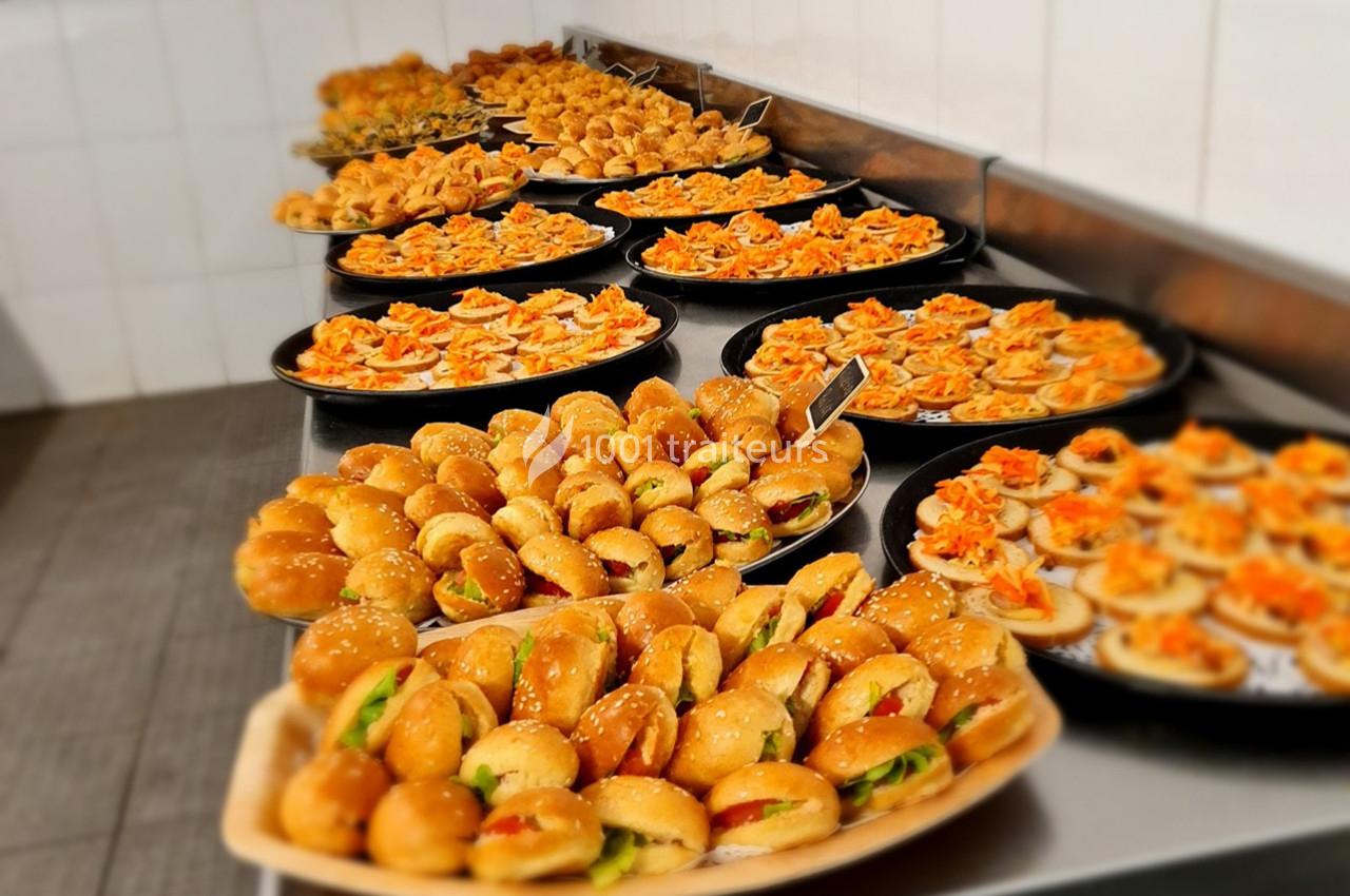 Plateaux garnis de mini-sandwichs et amuse-bouches disposés sur une table dans une cuisine professionnelle.