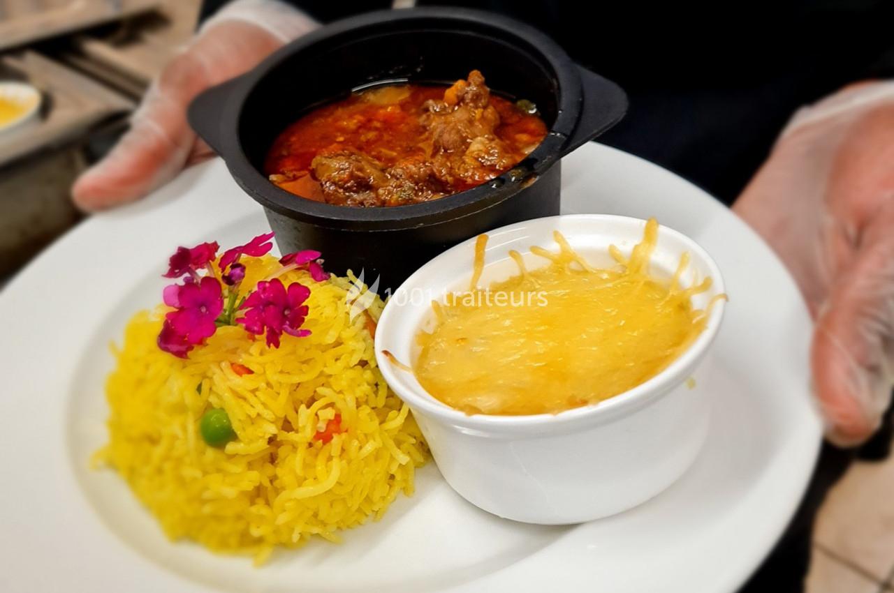 Assiette avec riz jaune garni de fleurs comestibles, gratin au fromage et ragoût servi dans un bol noir.