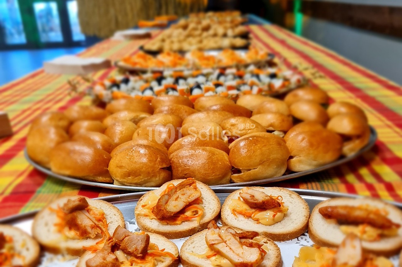 Plateaux de bouchées apéritives variées disposés sur une table recouverte d'une nappe colorée.